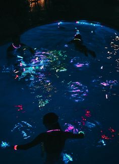 people are swimming in the pool at night with lights all around them and on their backs