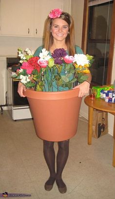 a woman is holding a large pot with flowers in it and smiling at the camera