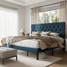 a bedroom with a large bed and blue headboard on the side, along with a footstool