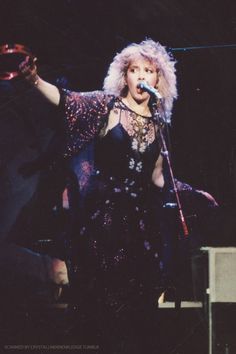 a woman in a black dress singing into a microphone