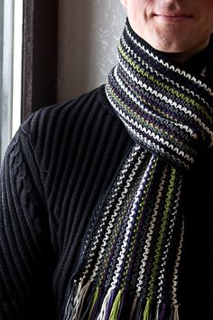 a man wearing a knitted scarf standing next to a window