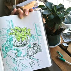 a drawing of a potted plant is held up in front of a table with pens and markers