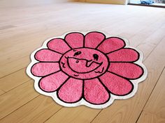 a pink rug with a smiling flower on the floor in front of a wooden floor