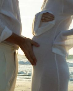 two people standing next to each other on a beach with the ocean in the background