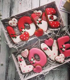 two decorated cookies in a box with the words love spelled out on them and hearts