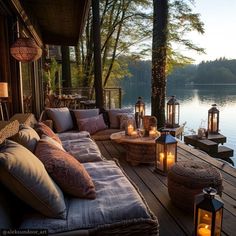 an outdoor deck with lots of pillows and lanterns on it, along with candles lit up