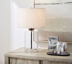 a glass table lamp sitting on top of a wooden dresser next to a framed photo