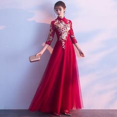 a woman in a long red dress standing against a wall with her hand on her hip