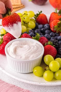 a plate with grapes, strawberries, and blueberries on it is being dipped into a bowl