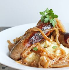 a white plate topped with meat and onions covered in gravy, garnished with parsley