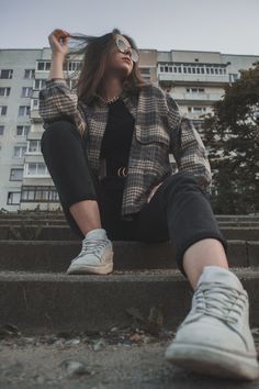 a woman sitting on the steps with her legs crossed and wearing white tennis shoes in front of an apartment building