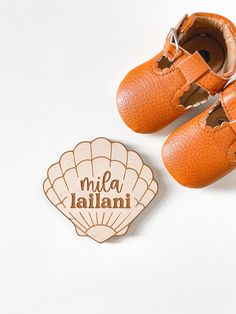 an orange pair of baby shoes next to a wooden shell with the word mia jallani written on it