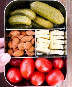 a person holding a container filled with assorted fruits and veggies next to cucumbers