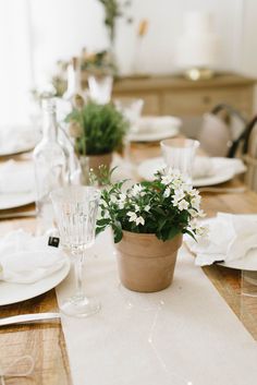 the table is set with white plates and flowers in a pot on top of it