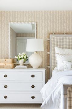 a white dresser sitting next to a bed in a bedroom under a mirror and lamp