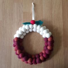 a christmas wreath made out of pom - poms on a wooden floor with a candle