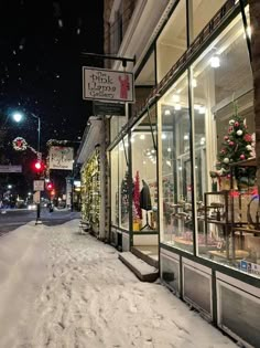 a snow covered street in front of a store with christmas decorations on the windows and lights