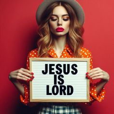 a woman holding a sign that says jesus is lord in front of her face and wearing a hat