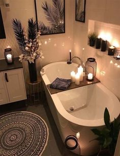 a bathtub with candles on the side and plants in it next to a rug