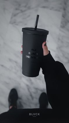 a person holding up a black cup with a straw in it