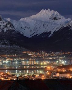 the mountains are covered in snow at night with lights on them and buildings lit up