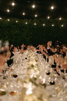 many people are sitting at a long table with wine glasses in front of their faces