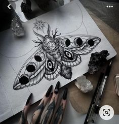 a woman's hand with black and white tattoos next to a drawing of a moth