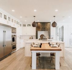 a large kitchen with white cabinets and wooden table surrounded by chairs in front of stainless steel appliances