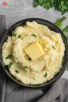 mashed potatoes with butter and parsley in a black bowl on a gray napkin