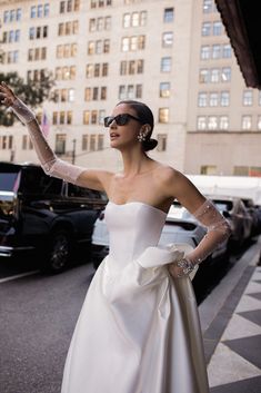 a woman in a white dress is standing on the street with her arms outstretched and wearing sunglasses