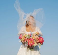 a woman in a wedding dress holding a bouquet of flowers with veil over her head