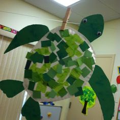 a paper plate turtle hanging from a string in an office cubicle decorated with green and white mosaic tiles