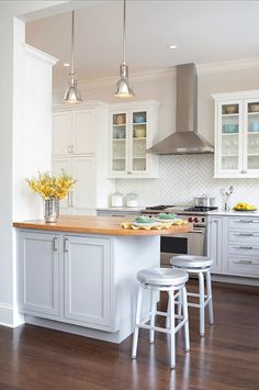 a kitchen with white cabinets and wooden flooring next to two stools in front of an island