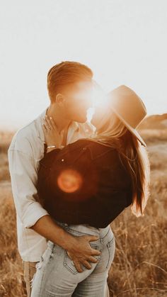 a man and woman kissing in a field with the sun shining down on them behind them