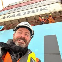 a man in safety gear standing next to a large blue and white sign that reads mahersak