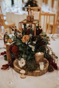 an arrangement of flowers and candles on a wooden stand at a table with white linens