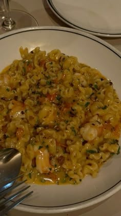 a white plate topped with pasta covered in shrimp and sauce next to silverware on a table