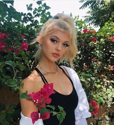 a woman with blonde hair wearing a black and white dress standing in front of flowers