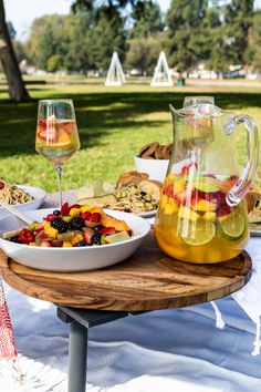 a bowl of fruit is next to a pitcher of wine on a table with plates and glasses