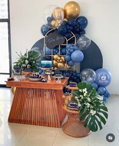 a table topped with balloons and cake on top of a wooden table next to a plant