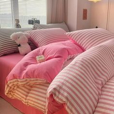 a bed with pink and white striped sheets, pillows and a teddy bear on it