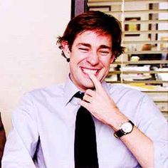 a man wearing a tie is smiling and holding his hand to his mouth while sitting at a desk