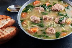 a bowl of soup with meatballs, carrots and spinach next to some bread