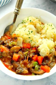 a bowl filled with mashed potatoes, meat and veggies next to a spoon