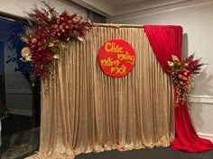 a stage set up with red and gold drapes, floral arrangements, and an orange sign