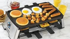 pancakes, eggs and sausages are cooking on a griddle in front of orange juice