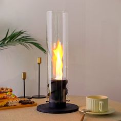 a table topped with a glass vase filled with fire next to a plate of food