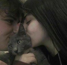 a man and woman kissing while holding a cat