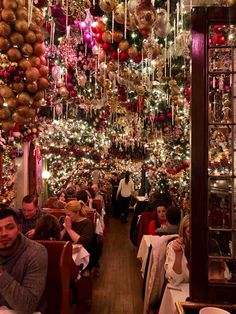 people sitting at tables in a restaurant with christmas decorations hanging from the ceiling and on the walls