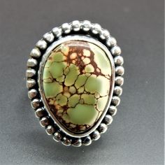 a ring with green and brown stones in it on a gray surface next to a black background